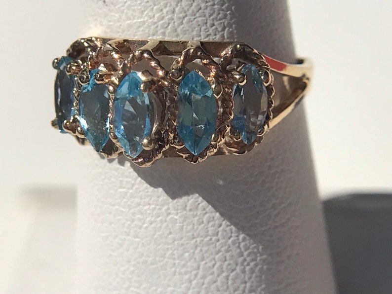 May include: A gold ring with five blue topaz stones set in a delicate, twisted band.