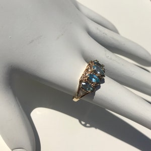 May include: A gold ring with five blue oval-shaped gemstones set in a delicate filigree design.