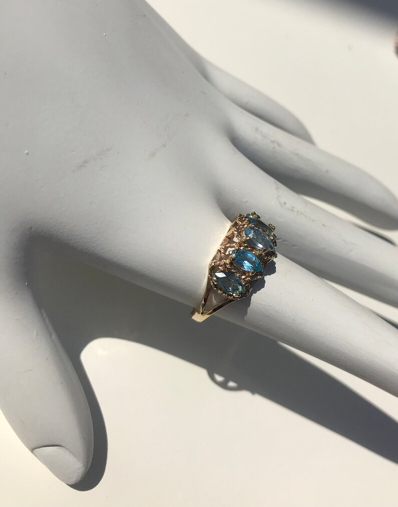 May include: A gold ring with five blue oval-shaped gemstones set in a delicate filigree design.