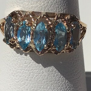 May include: A gold ring with five marquise-shaped blue topaz gemstones set in a delicate, twisted band.