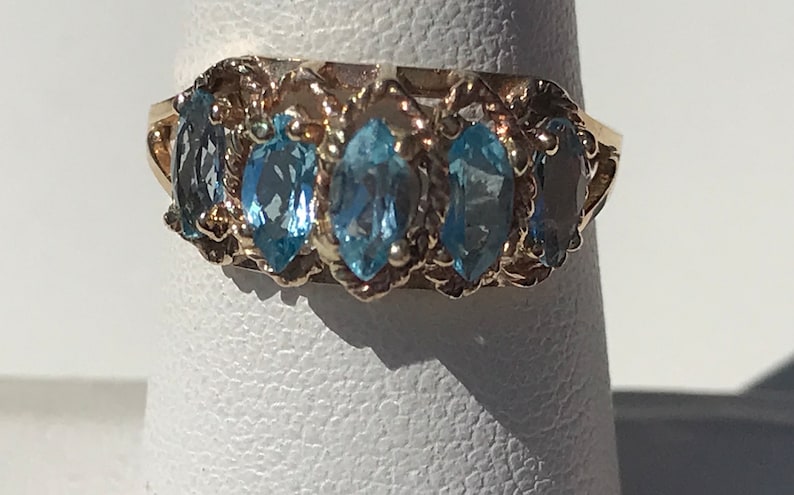 May include: A gold ring with five marquise-shaped blue topaz gemstones set in a delicate, twisted band.