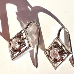 May include: A pair of silver dangle earrings with a clear cubic zirconia stone set in a square frame.