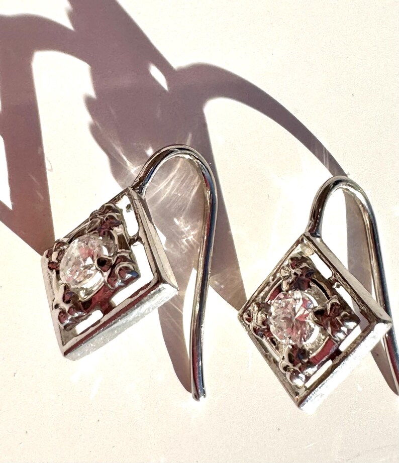May include: A pair of silver dangle earrings with a clear cubic zirconia stone set in a square frame.