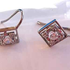 May include: A pair of silver earrings with a square design and a single clear stone in the center of each earring.
