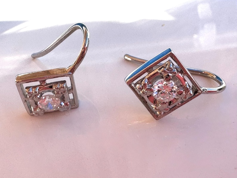 May include: A pair of silver earrings with a square design and a single clear stone in the center of each earring.