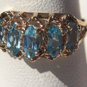 May include: A gold ring with a delicate, twisted band and five marquise-shaped blue topaz gemstones.