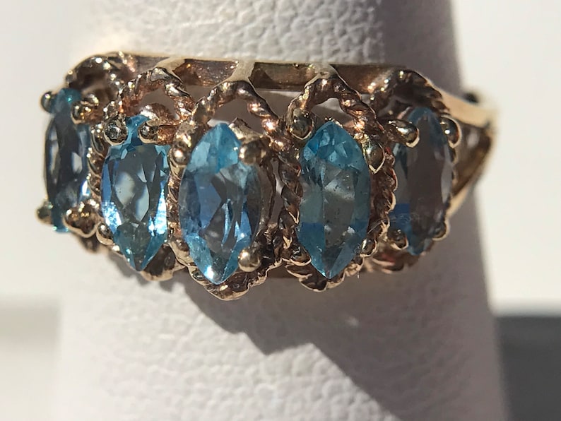 May include: A gold ring with a delicate, twisted band and five marquise-shaped blue topaz gemstones.