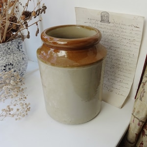 May include: A brown and white ceramic jar with a wide mouth. The jar has a brown glaze on the top and a white glaze on the bottom.