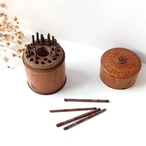 Puede incluir: Un portaherramientas cilíndrico de madera antigua con una parte superior perforada que contiene varias varillas de metal, acompañado de una tapa de madera a juego con el texto GEORGE H FAIRWEATHER y cuatro varillas sueltas.