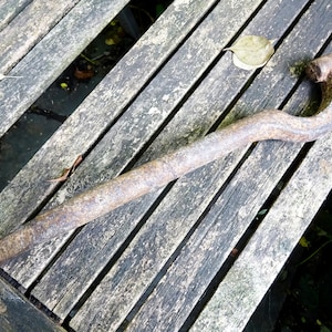 May include: A rusty metal wrench with a curved handle, lying on a wooden surface.