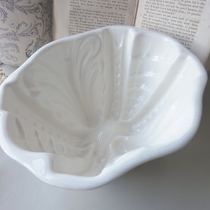 May include: White ceramic mold with a fluted design. The mold is shaped like a large, open flower.