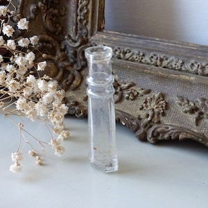 Puede incluir: Una botella de vidrio transparente con una superficie texturizada. La botella tiene una parte superior redondeada y una base cuadrada.