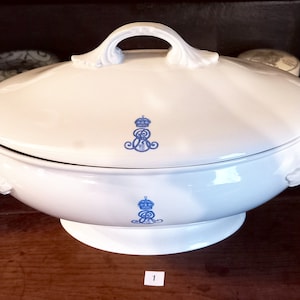 May include: White porcelain serving dish with a lid and two handles. The dish features a blue and white crest with a crown on top.