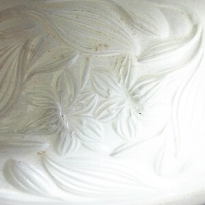 May include: A white ceramic oval serving dish with a floral embossed design. The raised relief pattern features stylized flowers and leaves. The dish has a smooth, glossy finish and is suitable for serving food.