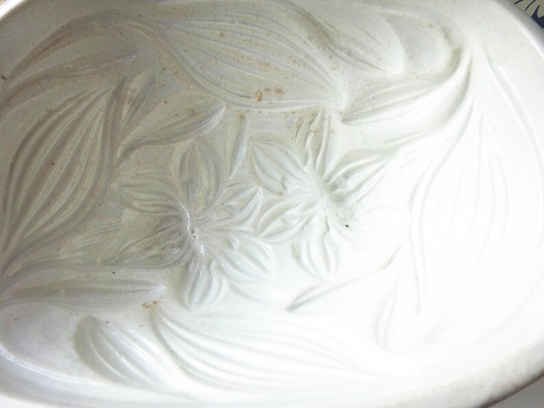 May include: A white ceramic oval serving dish with a floral embossed design. The raised relief pattern features stylized flowers and leaves. The dish has a smooth, glossy finish and is suitable for serving food.