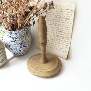 Puede incluir: Un rodillo de madera con una base redonda y un mango largo. El rodillo es de color marrón claro y tiene una superficie lisa.