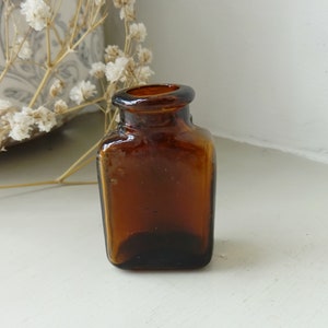 Peut inclure: Un petit flacon carré en verre ambré avec un dessus arrondi.