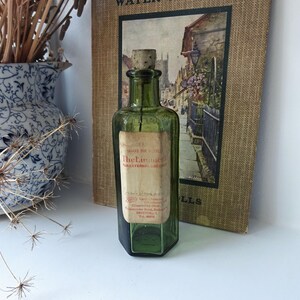 May include: A green glass bottle with a cork stopper and a label that reads "The Liniment for External Use Only". The label also includes the name and address of the manufacturer, "Boots Cash Chemists, Dispensing Dept, Gloucester Road, Bristol 7, Tel 20014".