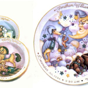 May include: Three decorative ceramic plates with baby-themed illustrations. The largest plate features a stork carrying a baby, a crescent moon, and a teddy bear in a carriage. The text on the plate reads "Jonathan William", "December 30, 1994", "9:59 am", "7 lbs. 9 oz", and "20 in". The smaller plates feature a teddy bear with a book and a rocking horse with a teddy bear.