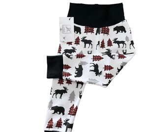May include: White baby leggings with a black waistband and a black and white print of moose, bears, and red and white plaid trees.