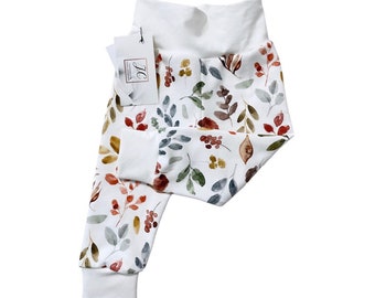 May include: White baby leggings with a watercolor print of leaves and berries in shades of red, orange, yellow, and green.