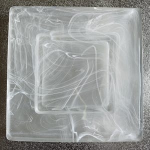 Könnte beinhalten: Eine weiße quadratische Glasschale mit einer kleineren quadratischen Schale im Inneren. Beide Schalen haben ein wirbelndes, marmoriertes Muster.