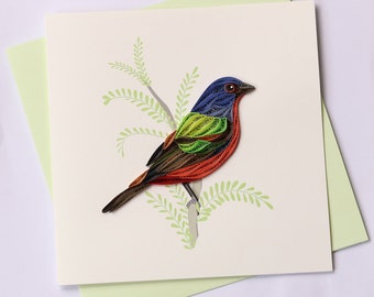 Op de afbeelding: Een kaart met een gequilde vogel, een Painted Bunting, met blauwe, rode, groene en bruine details, zittend op een tak met groene bladeren. De kaart ligt op een lichtgroene envelop.