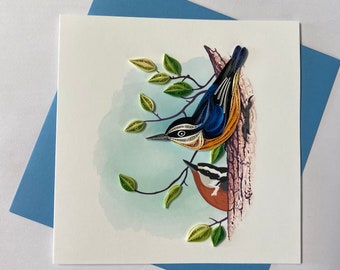 May include: A handmade paper quilling card featuring two birds perched on a tree branch. The birds are blue, orange, and black with intricate details. The background is a watercolor wash of blue and green.