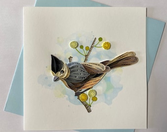 May include: A paper quilling art card featuring a brown and gray bird perched on a branch with yellow flowers. The bird is made of paper curls and the background is a watercolor wash.