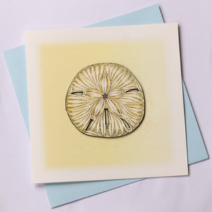 May include: A yellow card with a white border and a detailed illustration of a sand dollar in the center.