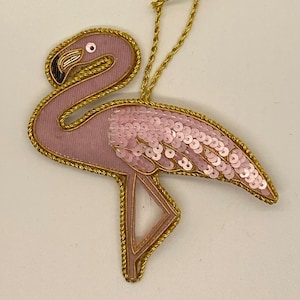 Peut inclure: Ornement de Noël en forme de flamant rose avec des bordures dorées et des paillettes roses.