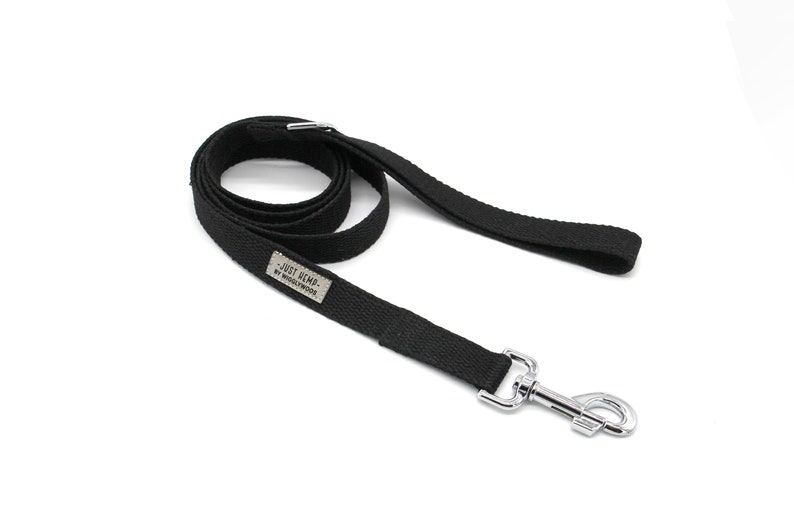 May include: Black dog leash with a silver metal clasp. The leash is made of a durable, woven material and features a small rectangular tag with the text "JUST HEMP. BY WIGGLYWOODS". The leash is coiled and ready for use.