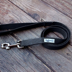 May include: A dark gray dog leash with a silver-colored metal clasp and handle. The leash is made of a woven fabric and has a small white tag with the text "Wiggles & Co" and a paw print logo.