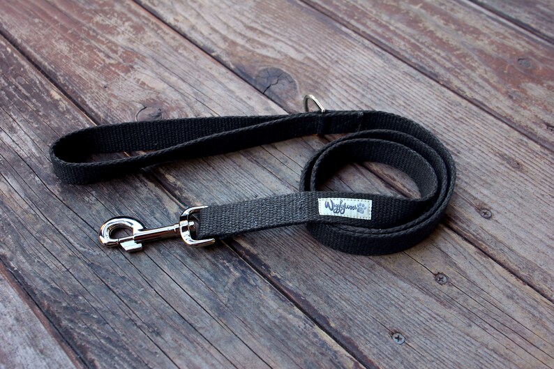 May include: A dark gray dog leash with a silver-colored metal clasp and handle. The leash is made of a woven fabric and has a small white tag with the text "Wiggles & Co" and a paw print logo.