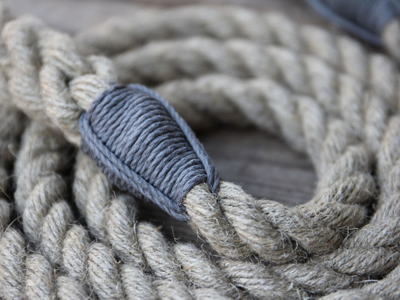 May include: Close-up of a coiled, thick rope with a gray, wrapped section. The rope is a natural beige color, with a textured, braided appearance. The gray section is tightly wound, creating a contrasting detail.