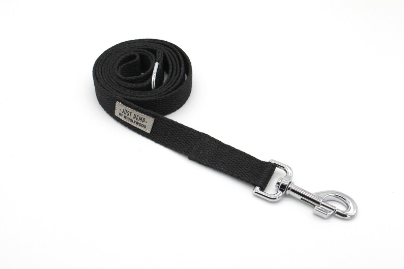 May include: A black dog leash made of woven material with a silver metal clasp. The leash is rolled up and has a small rectangular tag that reads "- JUST HEMP - BY WIGGLYWOODS."