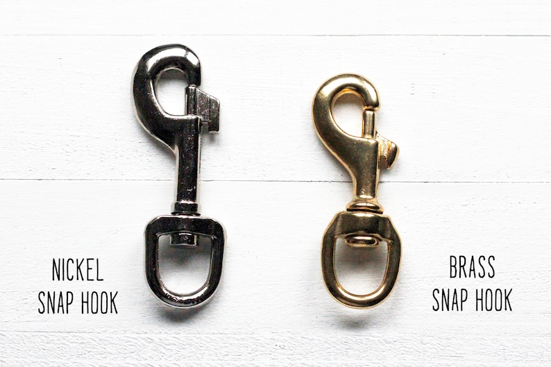 May include: Two snap hooks, one nickel and one brass, displayed side-by-side. The nickel snap hook is silver-colored, while the brass snap hook has a gold finish. Text below each hook identifies them as "NICKEL SNAP HOOK" and "BRASS SNAP HOOK."