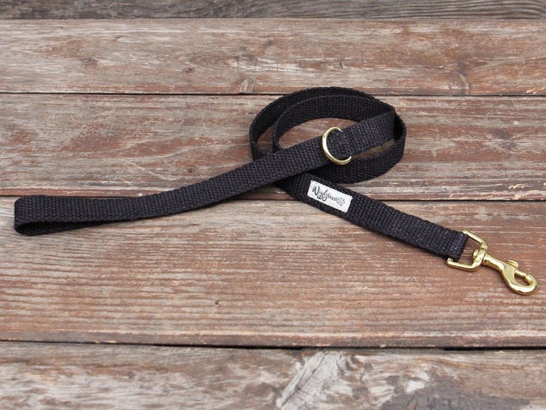 May include: A black dog leash with a brass-colored swivel clasp and a matching brass-colored ring. The leash is made of a woven material and has a small white tag with black text.