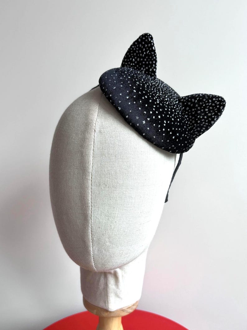 May include: A black cat ear headband with silver glitter accents. The ears are upright and attached to a thin black headband. The accessory is displayed on a mannequin head.