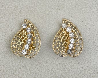 May include: A pair of gold-toned filigree earrings. Each earring has a teardrop shape with an openwork design and a row of clear, sparkling stones. The earrings are set against a neutral background.