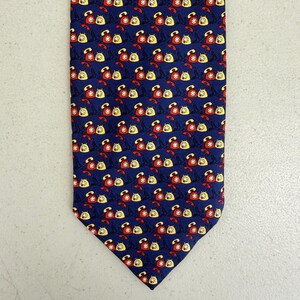 Puede incluir: Una corbata azul marino con un patrón repetido de teléfonos vintage rojos y amarillos. Cada teléfono tiene un diseño de estrella blanca. La corbata está hecha de un material liso, probablemente seda.