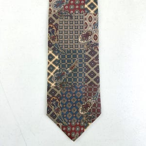 May include: A patterned necktie with a patchwork design. The tie features squares and paisley patterns in shades of red, blue, tan, and brown. The tie is made of a smooth fabric and is suitable for formal occasions.