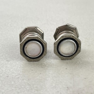 May include: A pair of silver cufflinks with a white mother-of-pearl center and a black border.