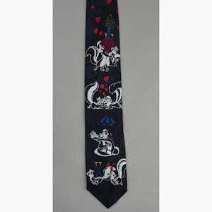 Puede incluir: Una corbata azul marino con mofetas de dibujos animados en varias escenas románticas. La corbata tiene corazones rojos y un árbol con bayas rojas. Las mofetas son en blanco y negro con detalles en rojo.
