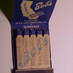 May include: A blue and white matchbook with the text "Bobi" and "BURBANK GLENDALE" printed on the front. The back of the matchbook lists the addresses for the Burbank and Glendale locations. The matchbook contains matches with the text "We Consume Annually", "75 tons Hamburger", "5000 gals. Mayonnaise", "10 tons Major Coffee", and "2,000,000 Baked Buns".