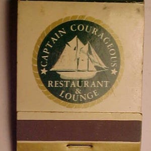 May include: Vintage matchbox featuring a nautical design. The matchbox has a cream-colored background with a circular emblem that reads "CAPTAIN COURAGEOUS RESTAURANT & LOUNGE" around a sailboat illustration. The bottom section is brown with a gold stripe.
