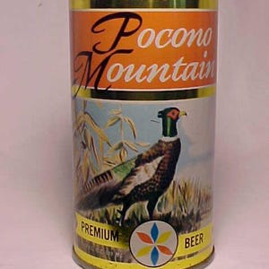 May include: A vintage aluminum can of Pocono Mountain Premium Beer. The can features a colorful illustration of a pheasant in a field of tall grass. The text "Pocono Mountain" is printed in a stylized font on the can, along with the words "Premium Beer".