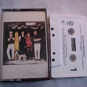 May include: A vintage cassette tape of The B-52's album "Whammy!" The album cover features a band photo with the album title. The white cassette tape is next to the cassette case.