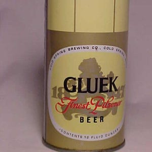 May include: Vintage Gluek Beer can with a yellow and brown color scheme. The can features the text "GLUEK Finest Pilsener BEER" in black and red script. The can contains 12 fluid ounces.