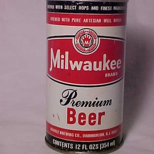 May include: A vintage aluminum can of Milwaukee Premium Beer. The can is red, white, and blue with a black and white logo of a crown and the letter M. The can reads "Brewed with Select Hops and Finest Ingredients" and "Brewed with Pure Artesian Well Water". The can also reads "Milwaukee Brand" and "Premium Beer". The can is 12 fluid ounces (354 ml).